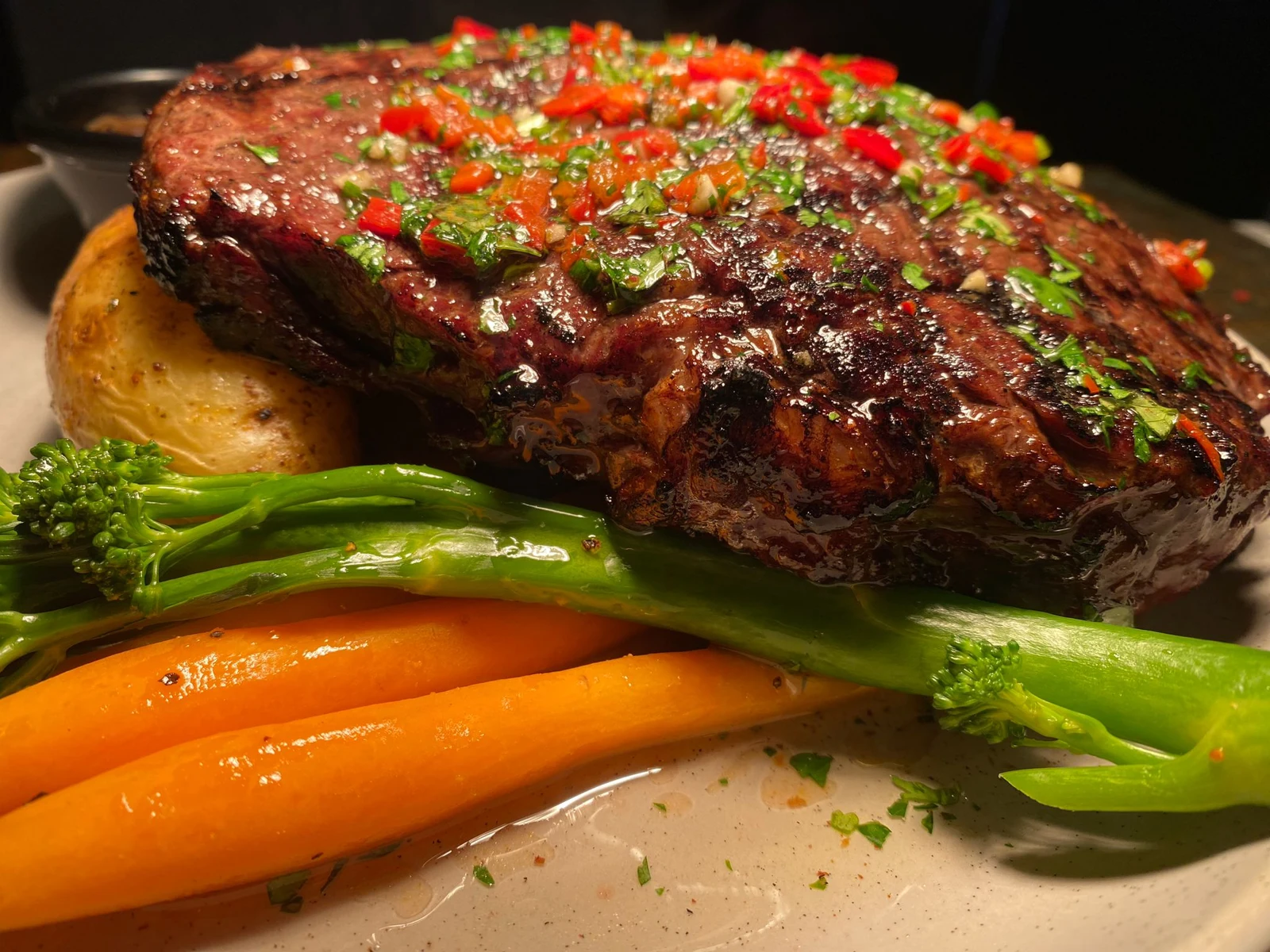 Grilled steak topped with herbs and red peppers, served with vegetables